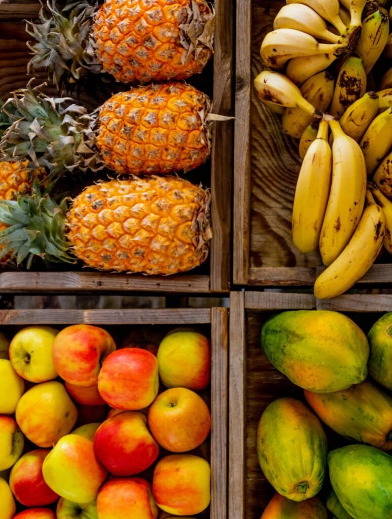 Colorful display of apples, pineapples, bananas, and papayas in wooden crates at a market.