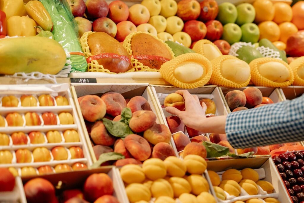 A colorful variety of fresh fruits at a market stand with a hand selecting a peach.